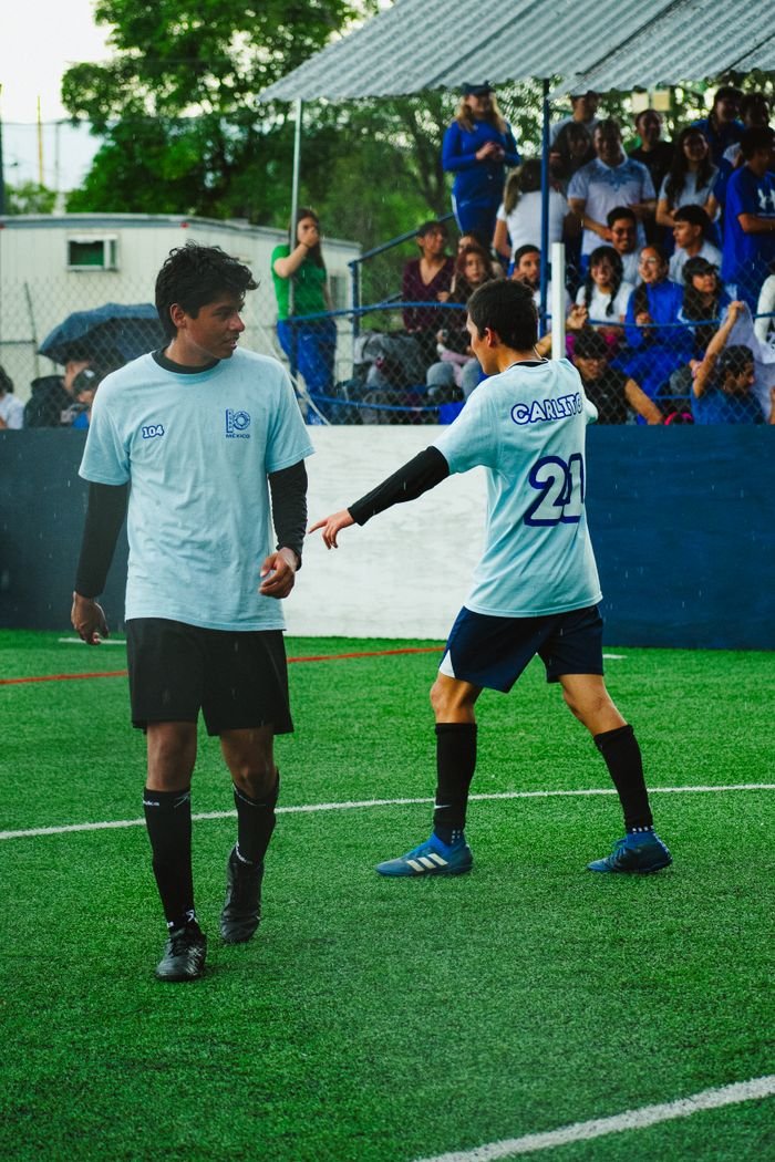 Young athletes playing football on a field in Mexico City with a cheering crowd.